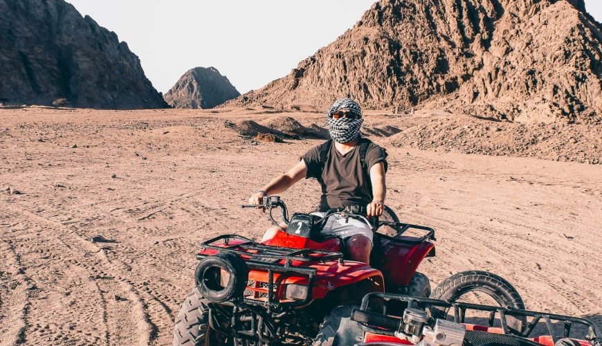 man riding red atv on brown sand during daytime